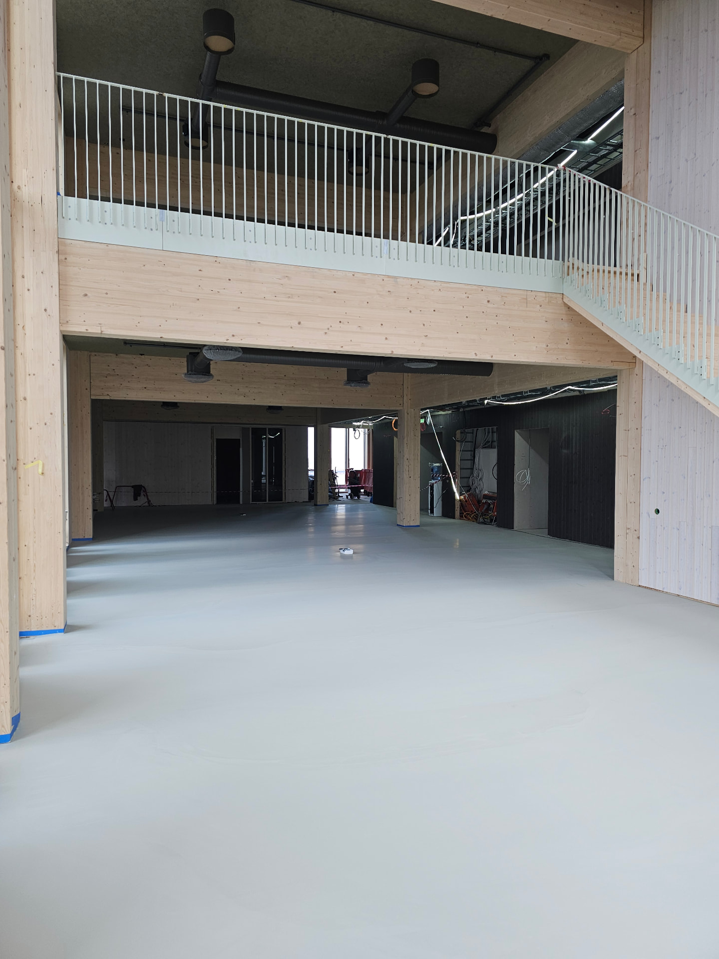 Double-height timber atrium at the Volvo Cars headquarters with the finished mineral floor below the mezzanine balustrade