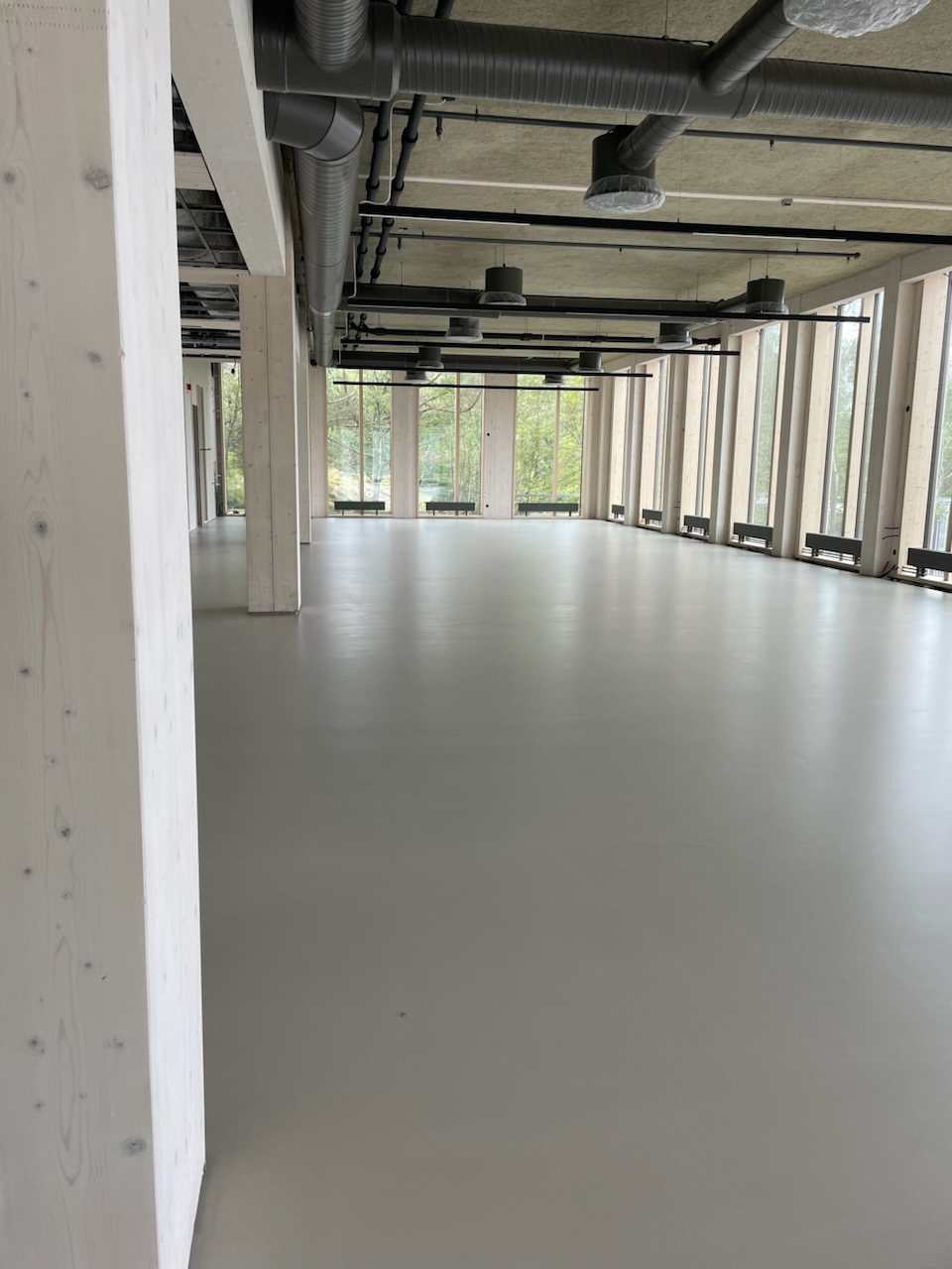 Seamless light-grey mineral floor running the length of an office floor at the Volvo Cars headquarters, between timber columns and perimeter windows