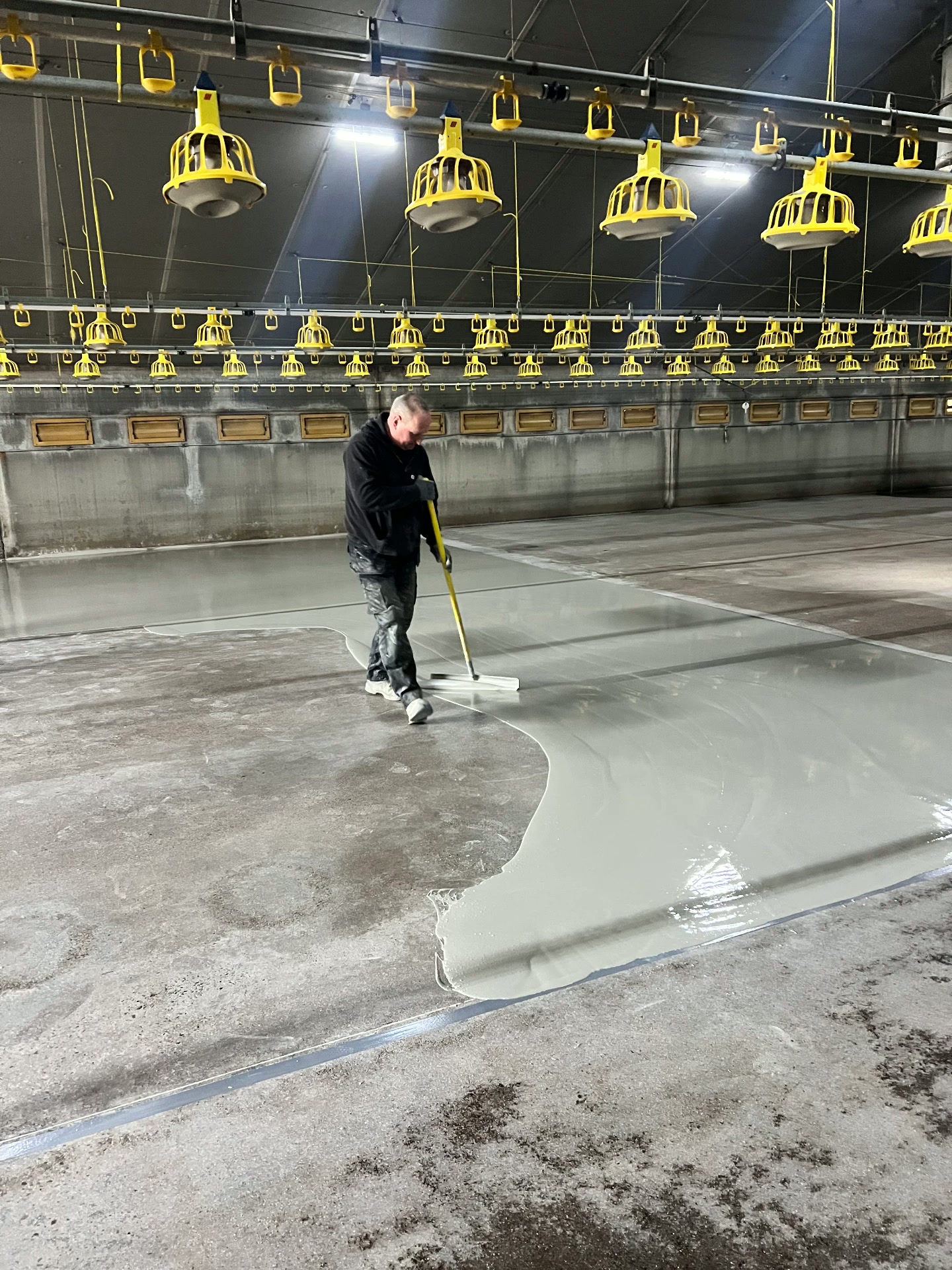 Applicator spreading the liquid mineral floor across the poultry house slab with a smoother