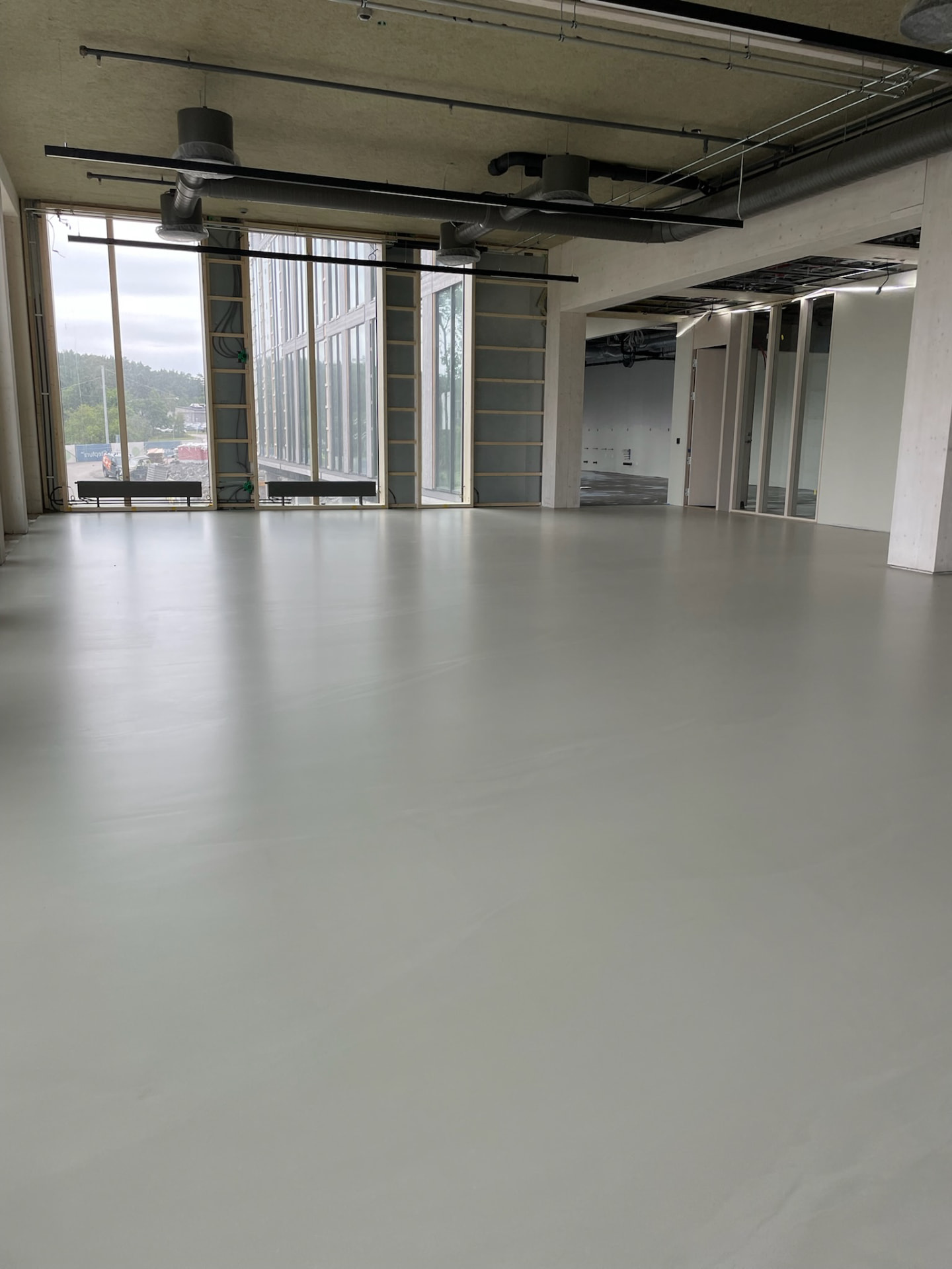 Finished seamless mineral floor across an office level at the Volvo Cars headquarters, with full-height glazing and an exposed technical ceiling