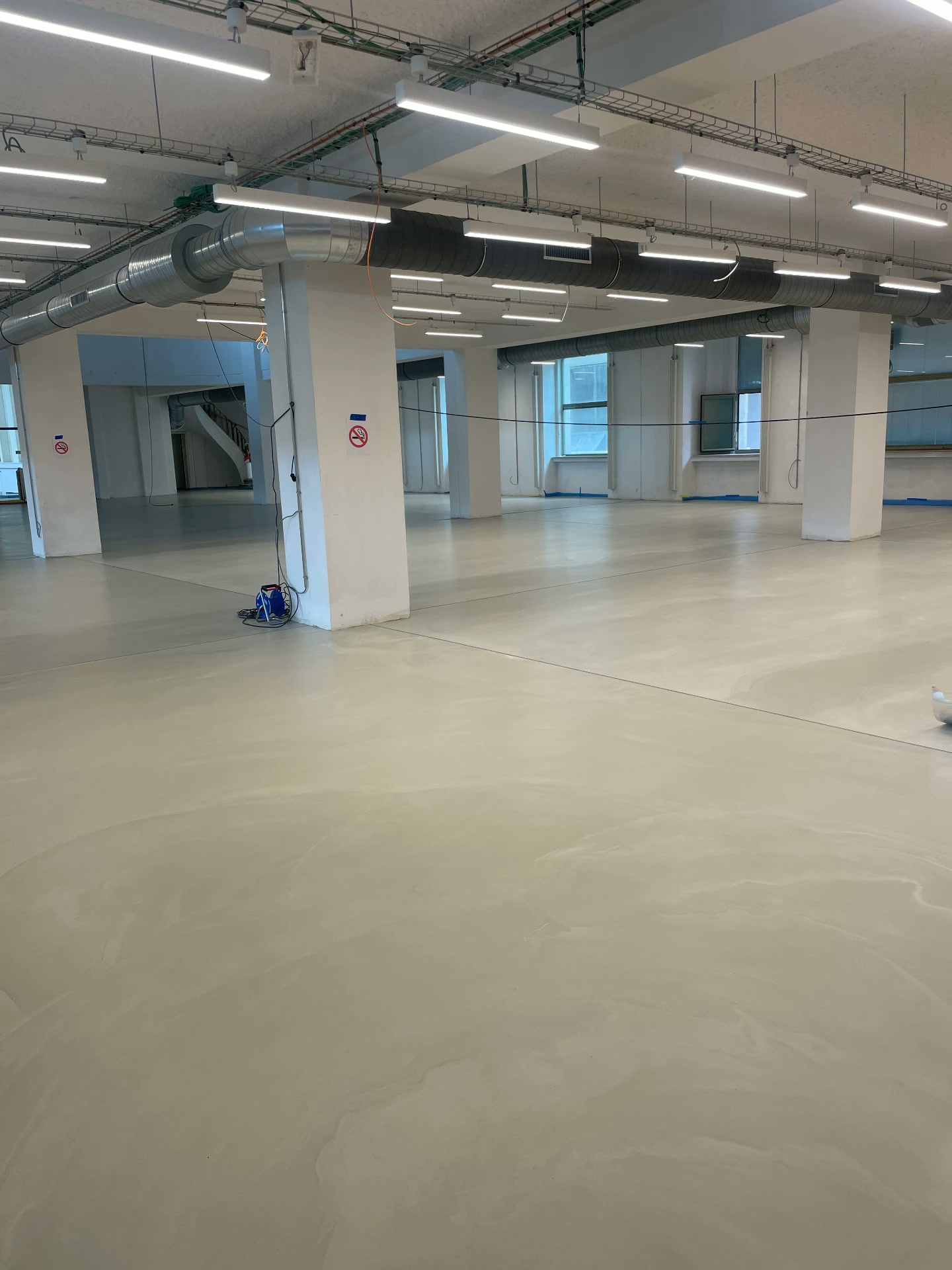 Finished seamless mineral floor running between white pillars under the industrial ceiling of the old Brussels-North station