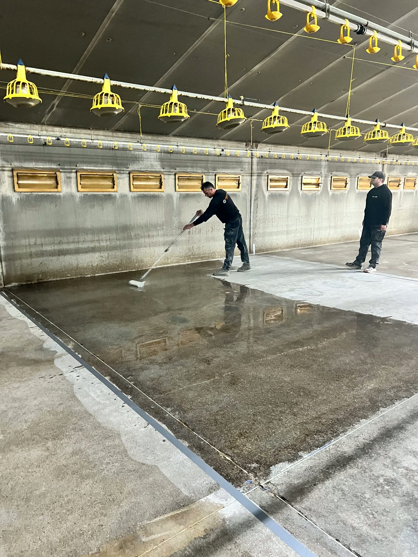 Technicians priming the concrete substrate of the poultry house before the mineral floor is poured