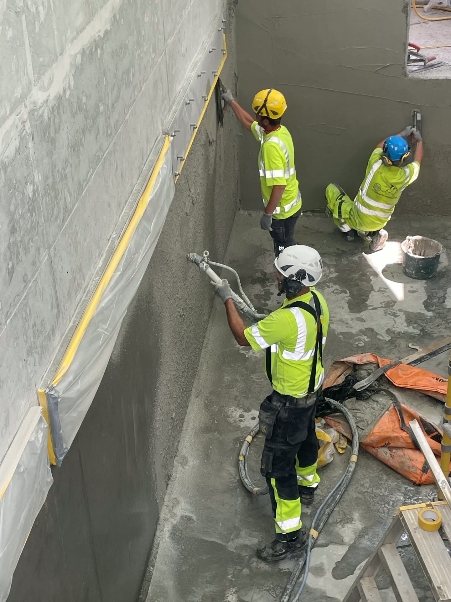 Applicators spray-applying and trowelling the mineral lining onto a concrete basin wall at Centrala Reningsverket, Kristianstad