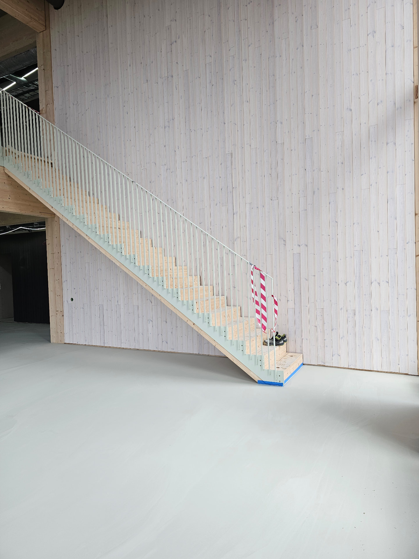 Timber staircase against a whitewashed timber wall at the Volvo Cars headquarters, with the seamless mineral floor in the foreground